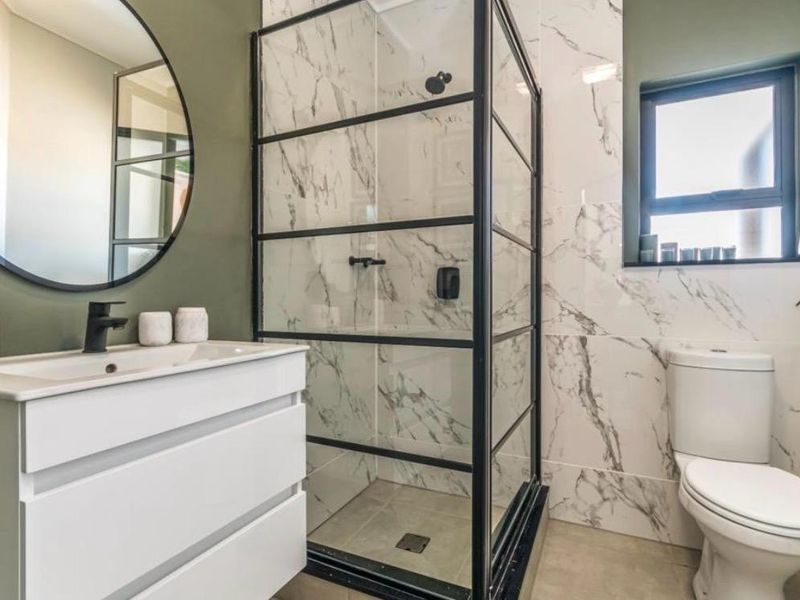 Modern bathroom featuring a sleek vanity, marble-look wall tiles, and a contemporary black-framed shower enclosure.