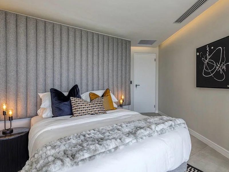 Modern bedroom featuring a textured upholstered feature wall, ducted air conditioning, and neutral tiled flooring in a well-maintained contemporary apartment.