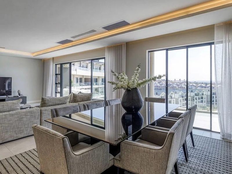 A modern open-plan living and dining area featuring high-end finishes, recessed ceiling lighting, ducted air conditioning, and expansive sliding glass doors with scenic views.