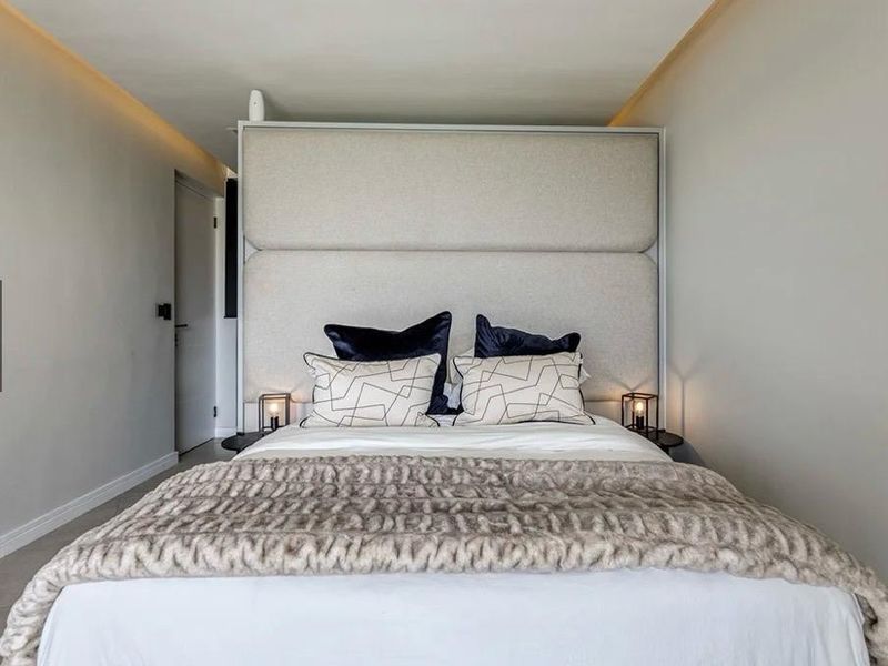 A modern bedroom featuring a large upholstered headboard and integrated recessed ceiling lighting, creating a clean and contemporary sleeping space.