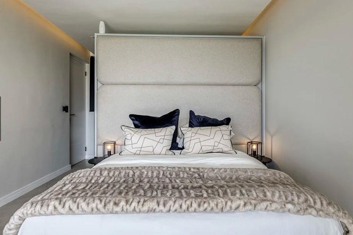 A modern bedroom featuring a large upholstered headboard and integrated recessed ceiling lighting, creating a clean and contemporary sleeping space.