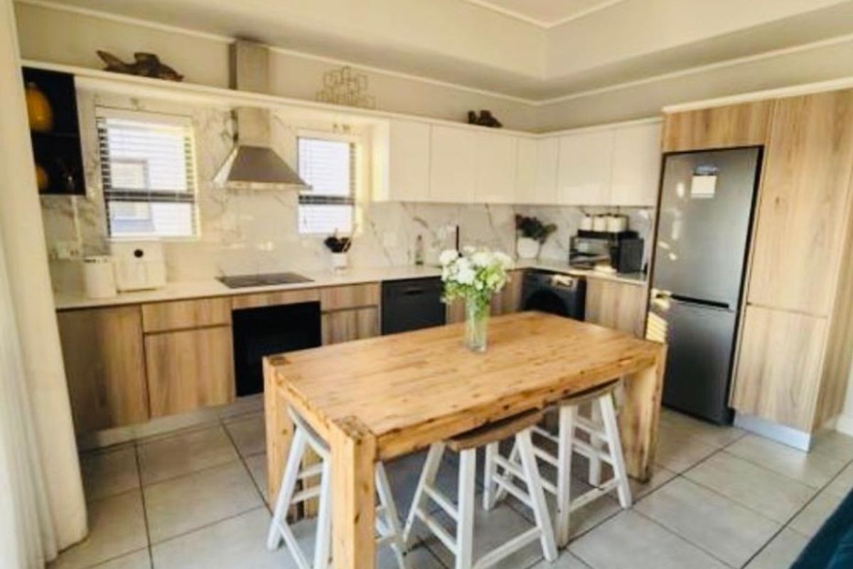 Modern kitchen featuring light wood-tone cabinetry, stone countertops, integrated appliances, and tiled flooring with a functional layout.