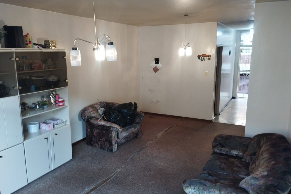 A living room area featuring carpeted flooring and dual pendant light fixtures, leading to an internal hallway.