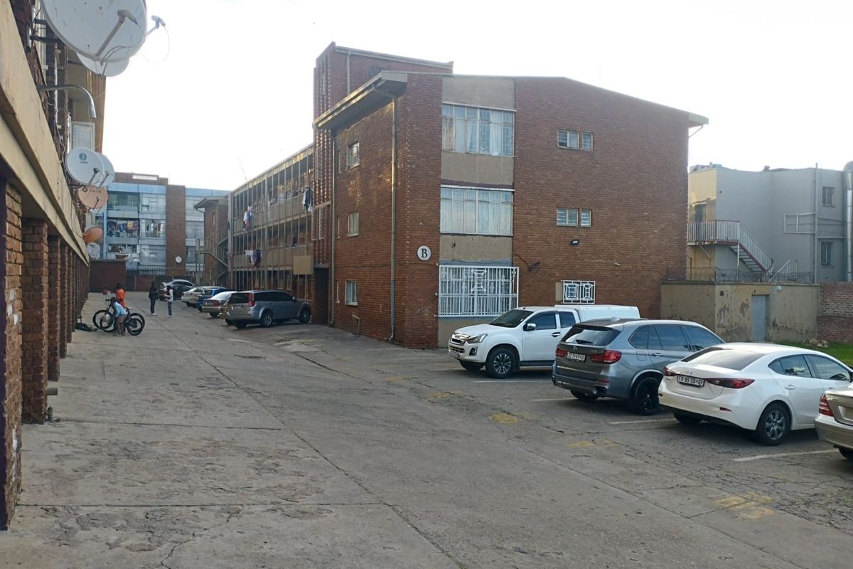 Exterior view of a multi-story brick apartment complex featuring a shared concrete parking area and communal walkways.