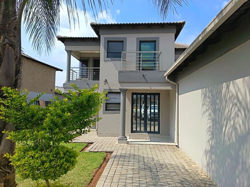 A well-maintained two-story rear exterior featuring a paved walkway, a balcony with modern stainless steel railings, and a secure entrance.