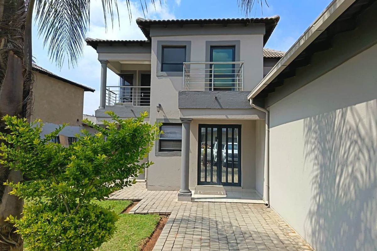 A well-maintained two-story rear exterior featuring a paved walkway, a balcony with modern stainless steel railings, and a secure entrance.