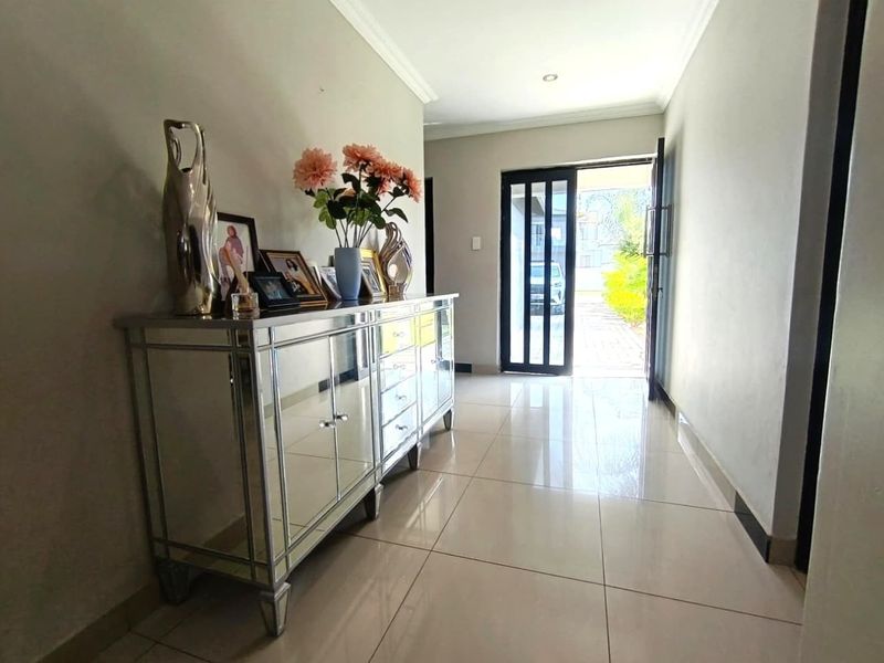 A bright and welcoming entrance hall featuring polished tiled flooring, recessed lighting, and a modern glass-panelled front door.