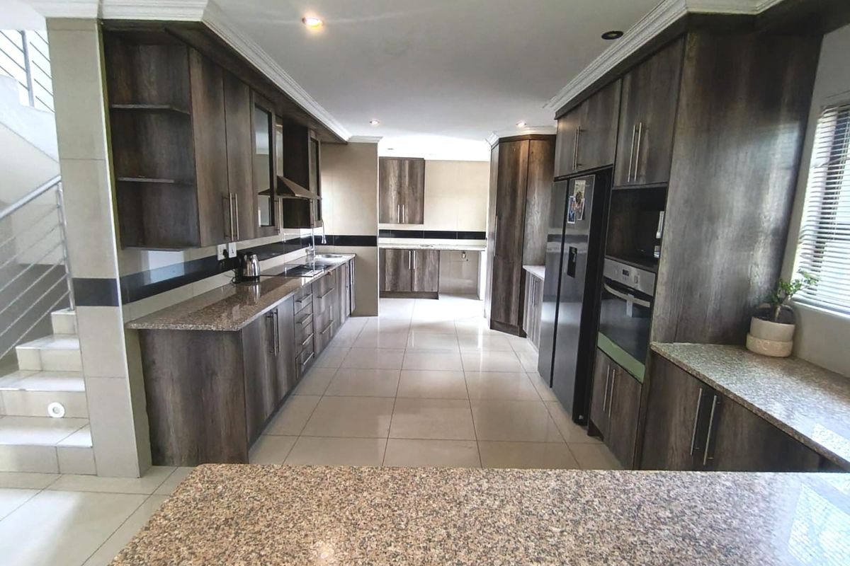 Spacious kitchen featuring dark wood cabinetry, granite countertops, built-in appliances, and tiled flooring, with an adjacent staircase leading to the upper level.