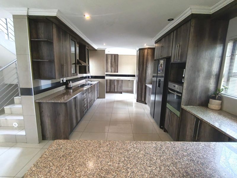 Spacious kitchen featuring dark wood cabinetry, granite countertops, built-in appliances, and tiled flooring, with an adjacent staircase leading to the upper level.