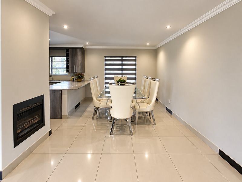 Spacious open-plan dining area featuring polished porcelain tiles, recessed fireplace, crown molding, and a modern kitchen with stone countertops.