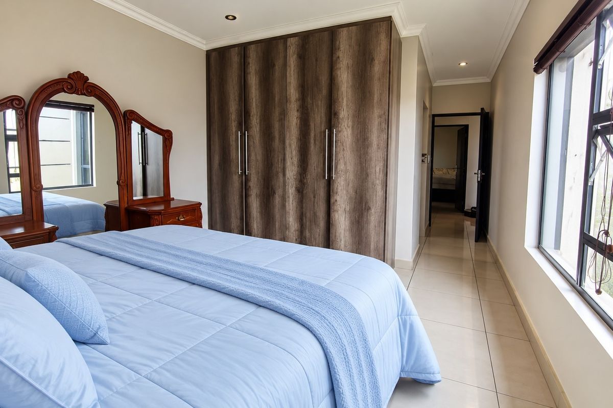 Spacious bedroom featuring built-in wooden cupboards, neutral tiled flooring, and recessed lighting, offering a clean and well-maintained living space.