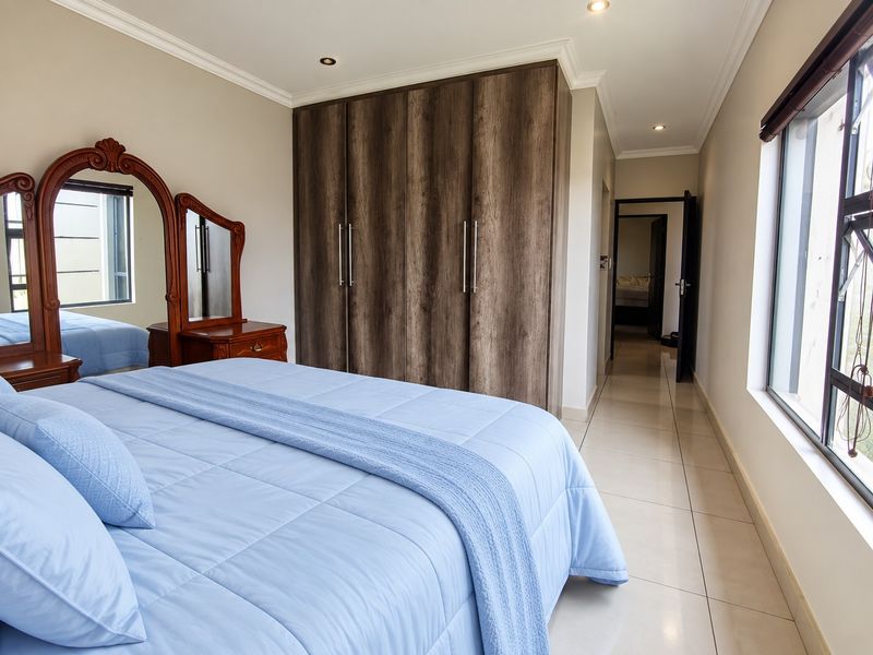 Spacious bedroom featuring built-in wooden cupboards, neutral tiled flooring, and recessed lighting, offering a clean and well-maintained living space.