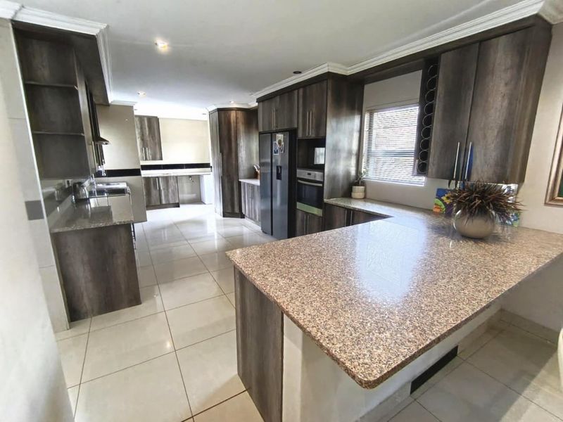 Spacious kitchen featuring dark wood cabinetry, granite countertops, built-in appliances, and tiled flooring with a functional layout.