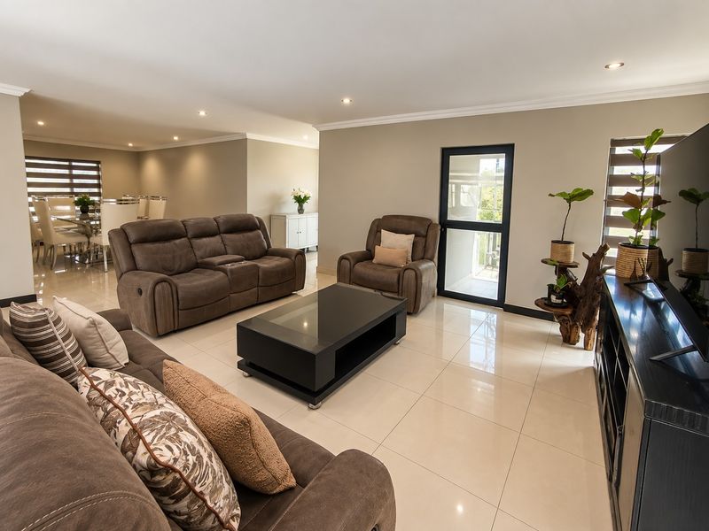 Spacious open-plan living and dining area featuring polished porcelain floor tiles, recessed downlighting, and direct access to an outdoor space via a glass door.