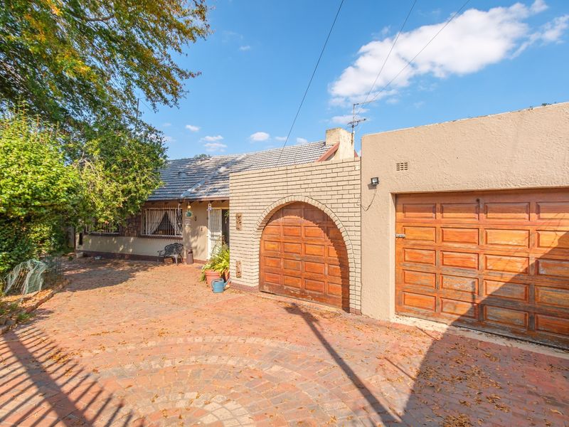 Front exterior view of the house featuring a brick driveway, arched entrance, and a wooden garage door with security bars on the windows.