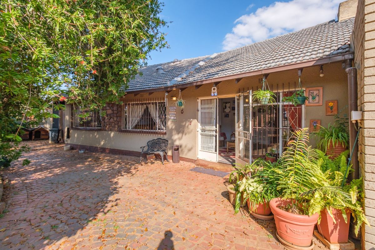 A rear exterior view of the house featuring a paved patio area, tiled roof, and security-fitted windows and doors.