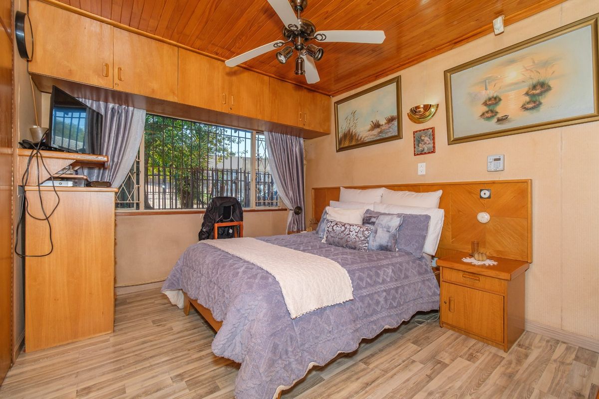 A bedroom featuring built-in timber cabinetry, a ceiling fan, and laminate flooring, with security bars installed on the window.