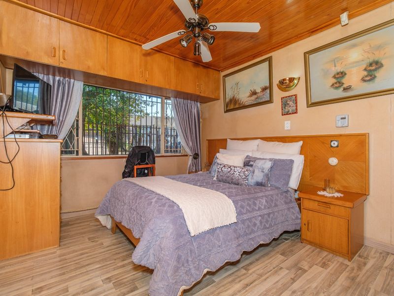 A bedroom featuring built-in timber cabinetry, a ceiling fan, and laminate flooring, with security bars installed on the window.