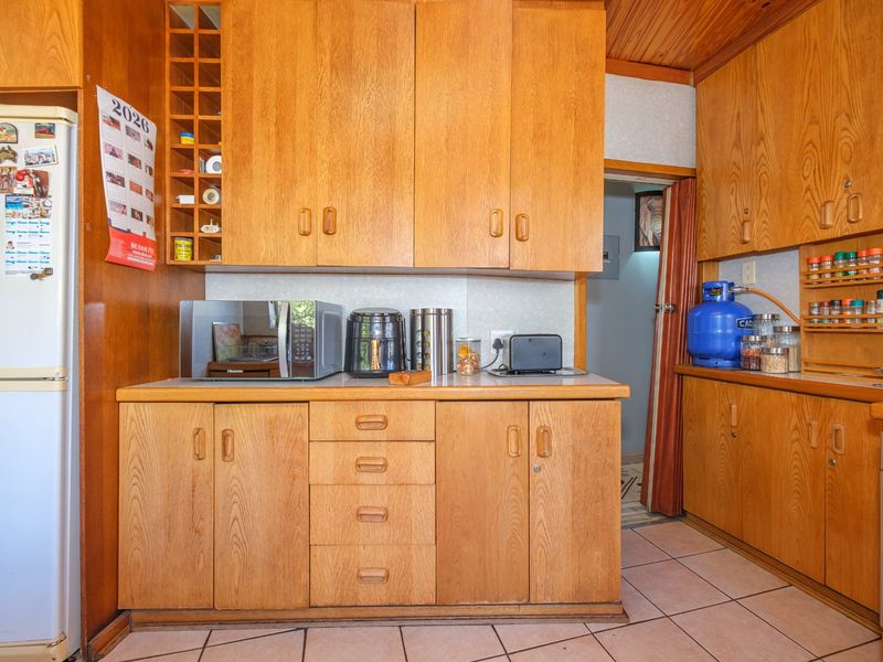 A functional kitchen featuring extensive wooden cabinetry, tiled flooring, a built-in oven, and a timber-clad ceiling, offering a traditional aesthetic.