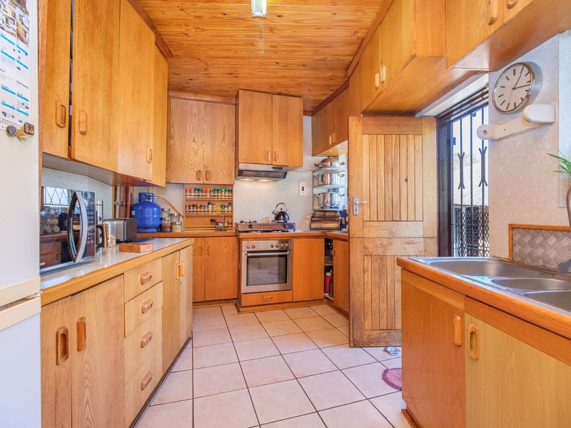 A functional kitchen featuring extensive wooden cabinetry, a tiled floor, a wooden ceiling, and built-in cooking appliances with direct access to the exterior.