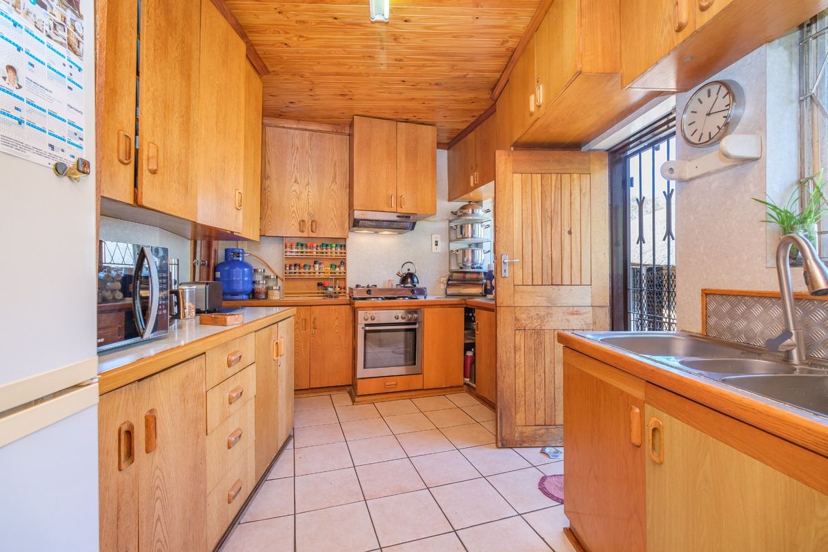 A functional kitchen featuring extensive wooden cabinetry, a tiled floor, a wooden ceiling, and built-in cooking appliances with direct access to the exterior.