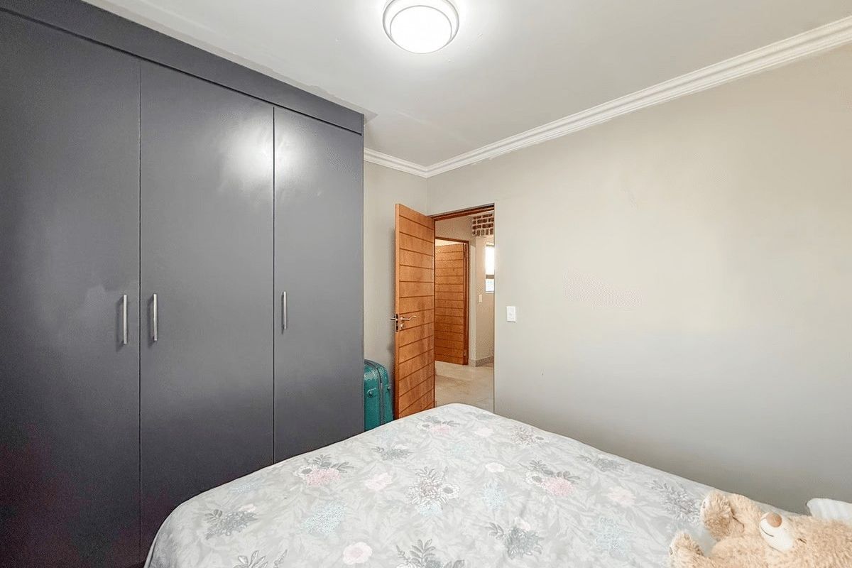 A well-maintained bedroom featuring dark grey built-in cupboards, neutral wall finishes, and decorative ceiling cornicing.