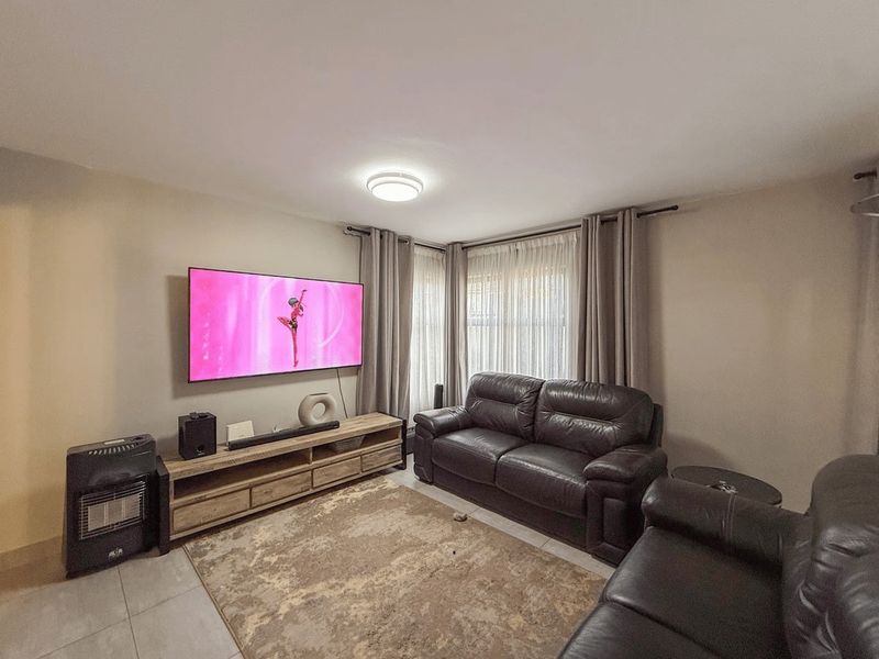A comfortable living room featuring tiled flooring, neutral wall tones, and large windows dressed with curtains, providing a functional and inviting space.