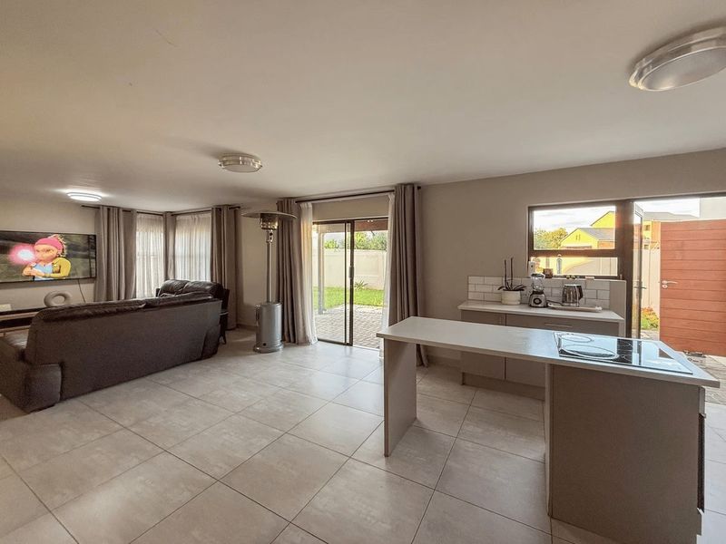 Open-plan living area featuring a modern kitchen with island, electric hob, tiled flooring, and sliding doors leading to the rear patio.