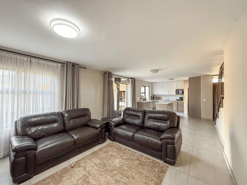 Open-plan living area featuring tiled floors, a modern kitchen with built-in cabinetry and island, and an adjacent staircase.