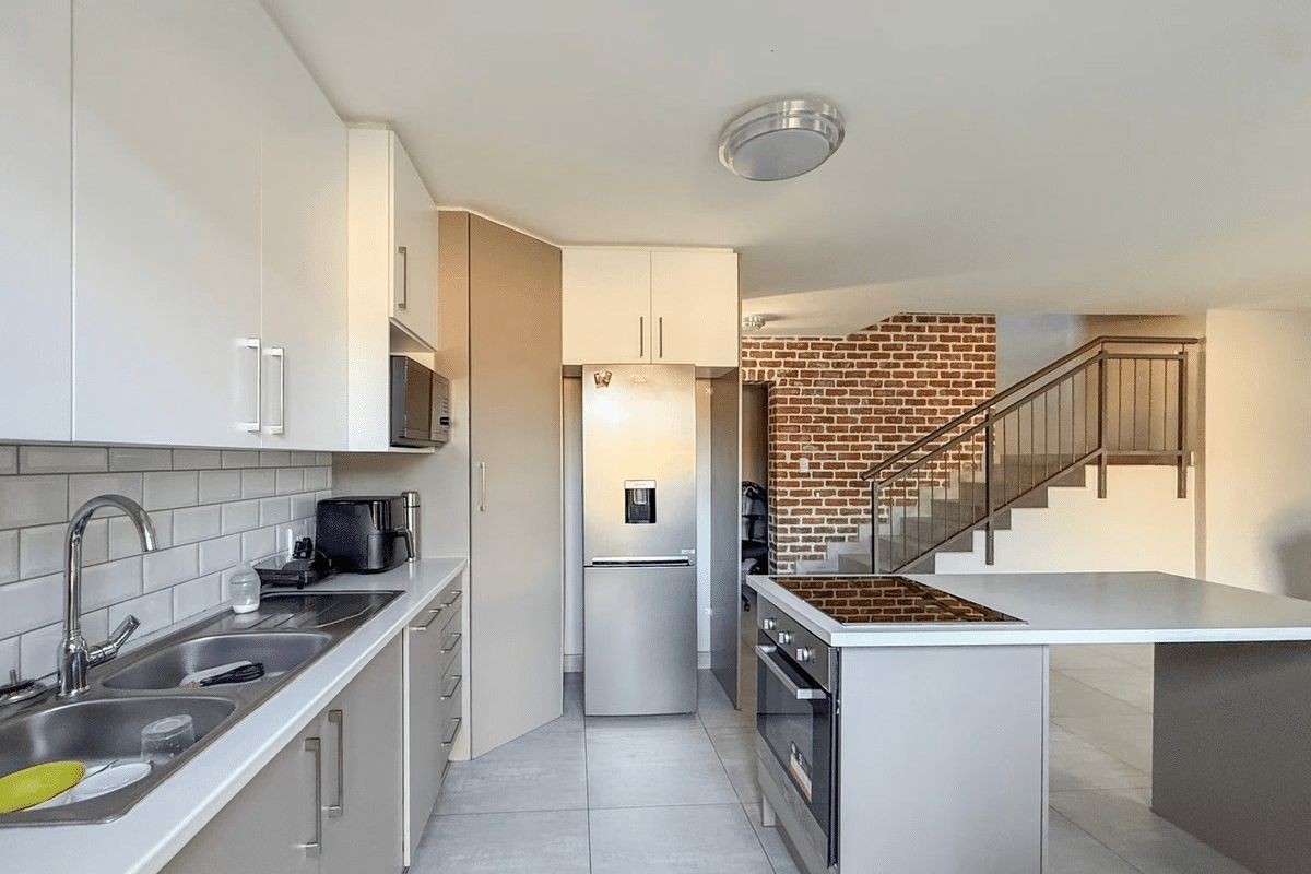 Modern kitchen featuring sleek cabinetry, subway tile backsplash, built-in oven and hob, adjacent to an exposed brick staircase.