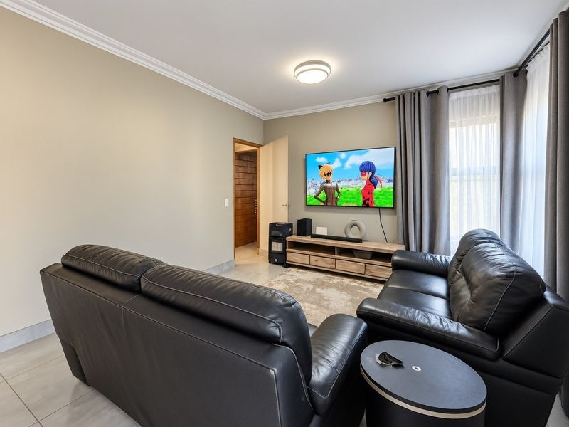 A well-maintained living room featuring neutral wall tones, crown molding, tiled flooring, and a wall-mounted television setup.