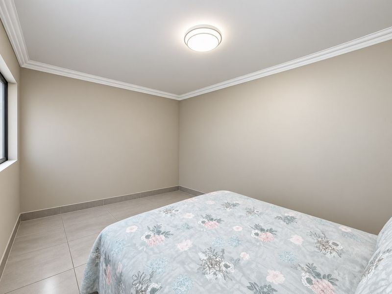 A clean, neutral-toned bedroom featuring large format floor tiles, crown molding, and a simple flush mount ceiling light fixture.