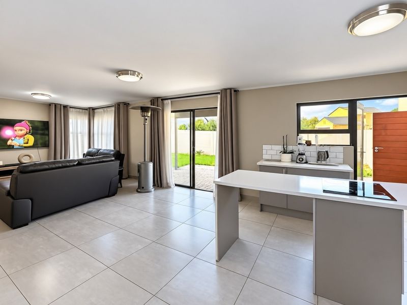 Modern open-plan living area featuring tiled floors, a functional kitchen island with a built-in hob, and seamless access to the outdoor patio.