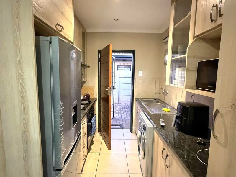Compact kitchen featuring light wood cabinetry, granite countertops, integrated appliances, and direct access to an exterior paved area.