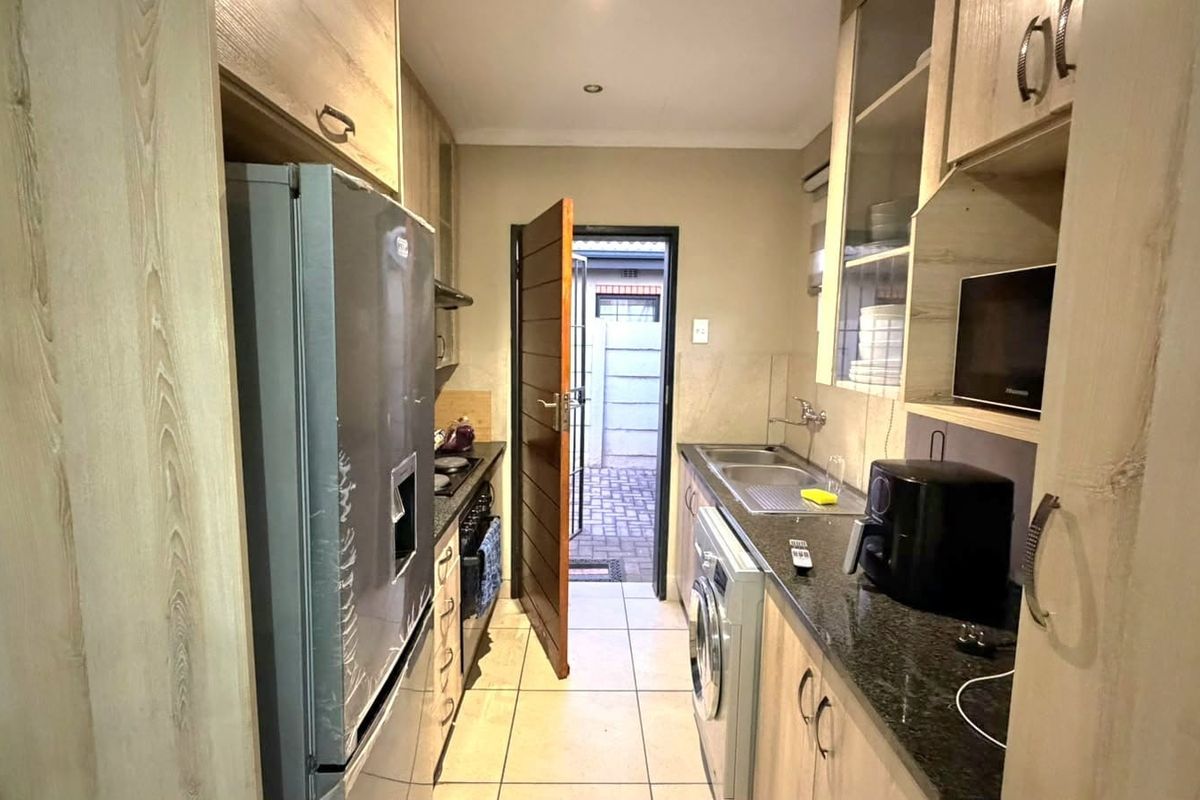 Compact kitchen featuring light wood cabinetry, granite countertops, integrated appliances, and direct access to an exterior paved area.
