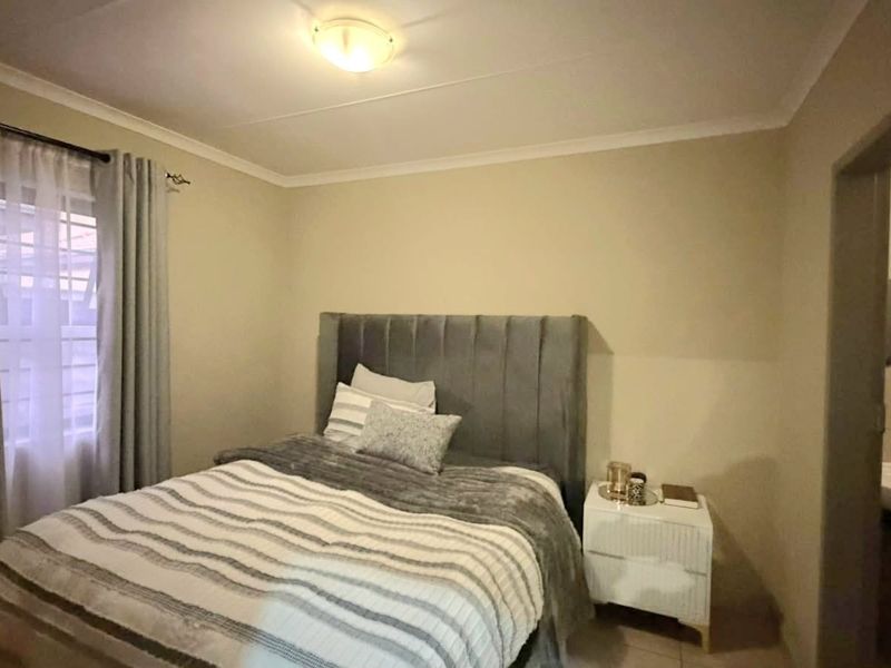A standard bedroom featuring neutral wall tones, tiled flooring, and an adjoining en-suite bathroom area.