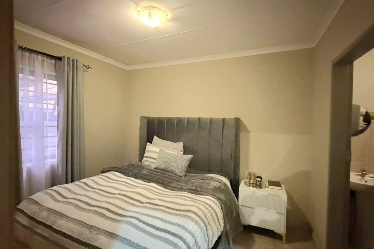 A standard bedroom featuring neutral wall tones, tiled flooring, and an adjoining en-suite bathroom area.