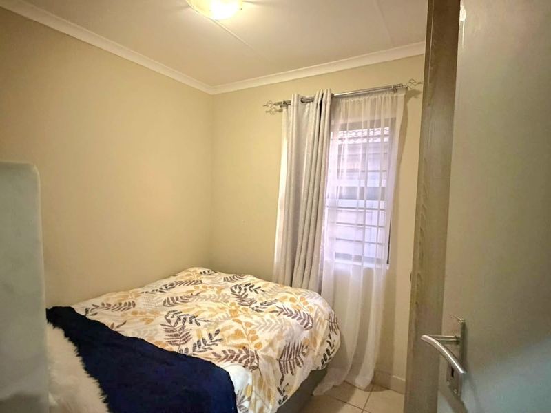 A compact bedroom featuring neutral walls, a window with curtain treatments, and a ceiling light fixture.