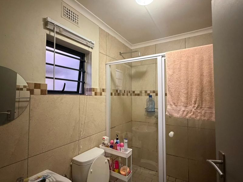 A functional bathroom featuring tiled walls, a shower enclosure, and a toilet, with a window providing natural light and ventilation.