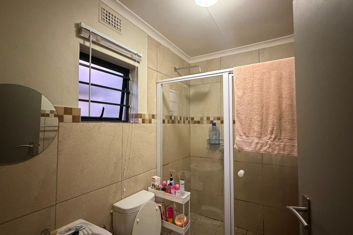 A functional bathroom featuring tiled walls, a shower enclosure, and a toilet, with a window providing natural light and ventilation.