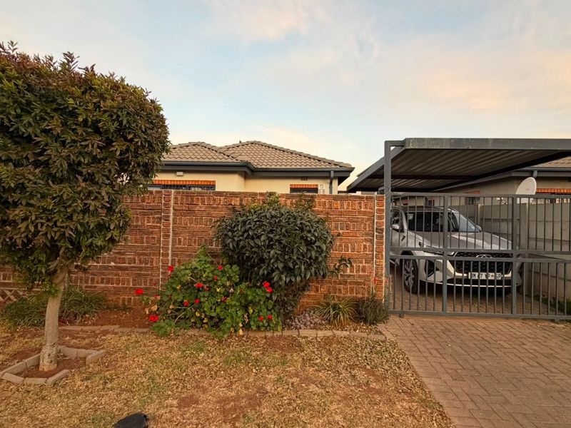 Front exterior view featuring a brick boundary wall, metal driveway gate, and a covered carport area.