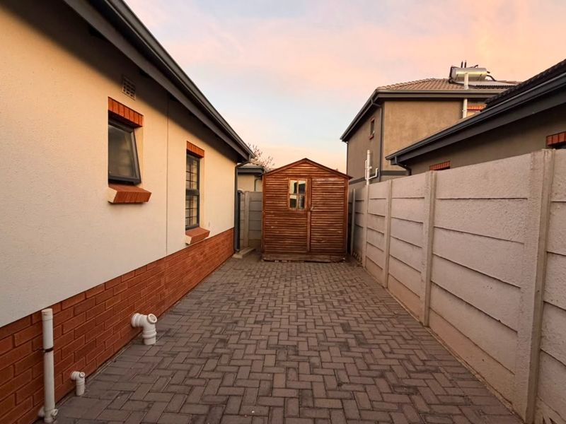A side exterior view of the property featuring paved ground, brick and plaster wall finishes, and a precast concrete boundary wall.