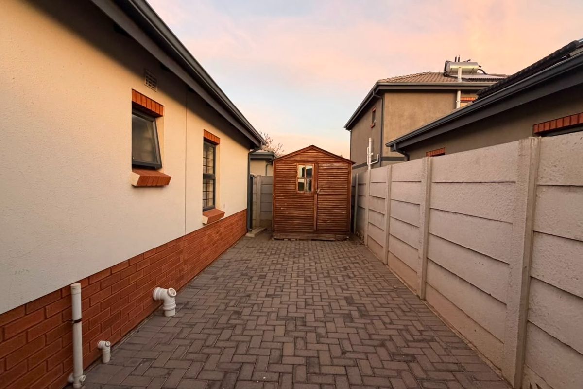A side exterior view of the property featuring paved ground, brick and plaster wall finishes, and a precast concrete boundary wall.