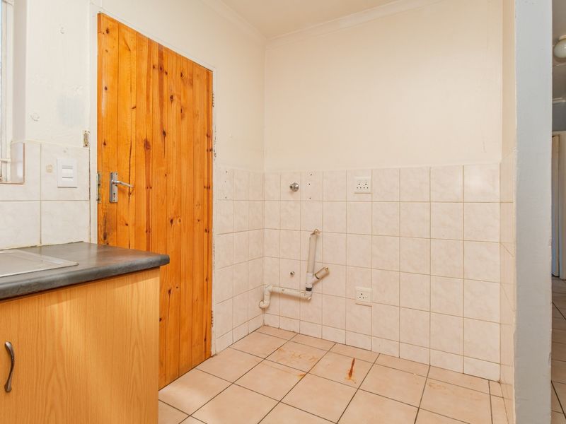 A functional laundry area featuring tiled walls and flooring, plumbing connections for appliances, and a wooden door leading to an adjacent space.