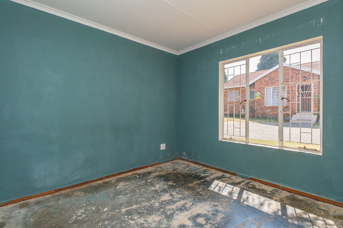 An empty bedroom featuring teal walls, security bars on the window, and flooring in need of replacement or refurbishment.