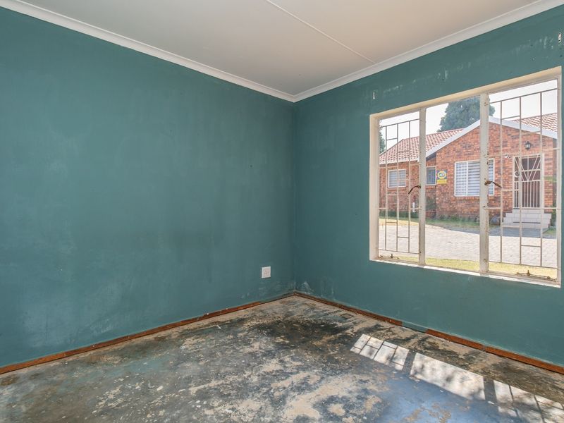 An empty bedroom featuring teal walls, security bars on the window, and flooring in need of replacement or refurbishment.