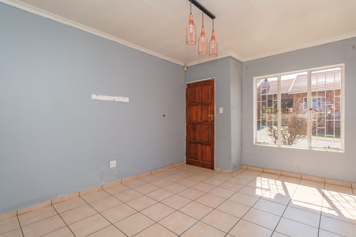 An empty living area featuring tiled flooring, a timber entrance door, and natural light through a window with security bars.
