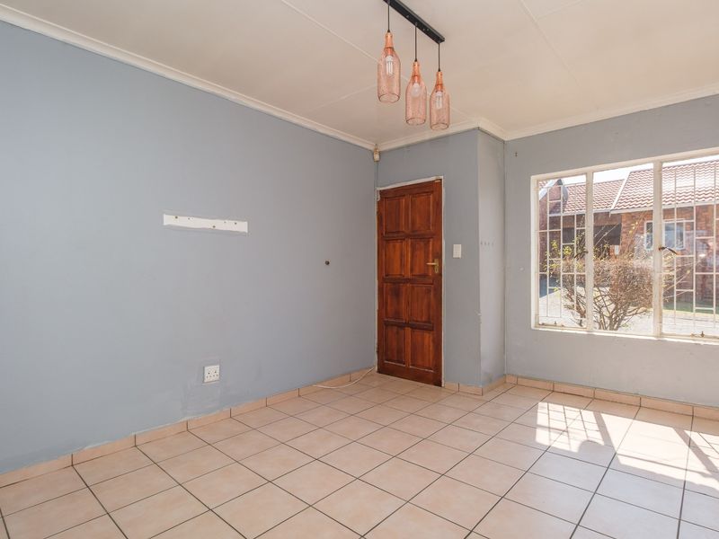 An empty living area featuring tiled flooring, a timber entrance door, and natural light through a window with security bars.