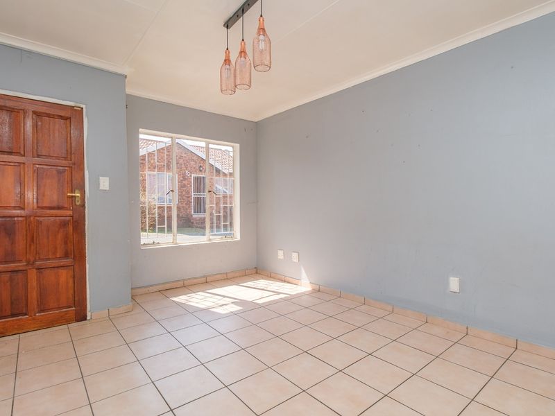 An empty dining area featuring neutral tiled flooring, light blue walls, and a modern pendant light fixture, offering a blank canvas for personalization.