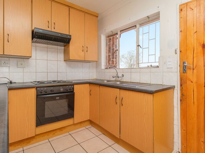 A functional kitchen featuring laminate cabinetry, built-in oven with hob, extractor fan, double sink, and tiled flooring with security bars on the window.